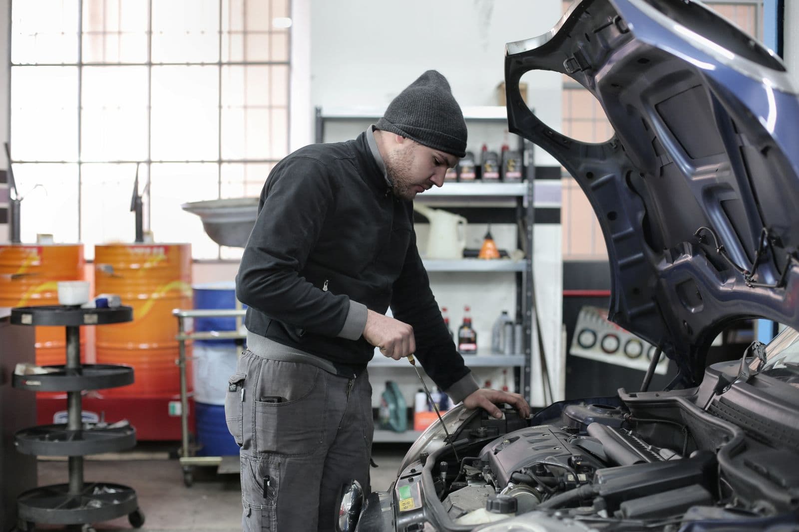 Mechanic checking oil under an open hood in an auto repair shop